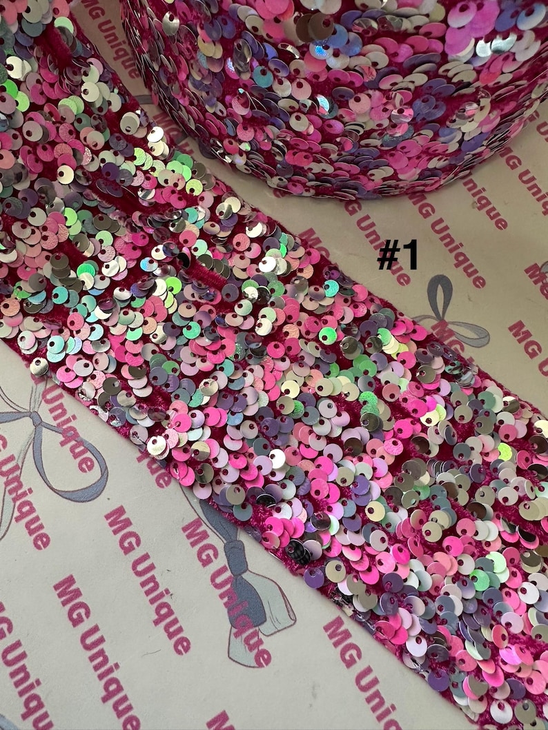 Op de afbeelding: Close-up van een rol roze paillettenstof met iriserende pailletten. De stof heeft een dieproze kleur en de pailletten zijn een mix van roze, zilver en iriserende kleuren. De tekst "#1" is zichtbaar.