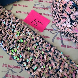 Op de afbeelding: Close-up van een donkerblauwe stof versierd met iriserende roze pailletten. Een roze label met het nummer 15 is zichtbaar. Geschikt voor knutselen of decoratie.
