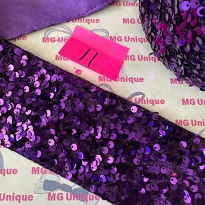 Op de afbeelding: Close-up van diverse paarse knutselbenodigdheden. Inclusief een breed paillettenlint, een satijnen lint en een bolletje paillettenmateriaal. Een roze prijskaartje met het nummer 11 is ook zichtbaar. De achtergrond heeft de tekst "MG Unique".