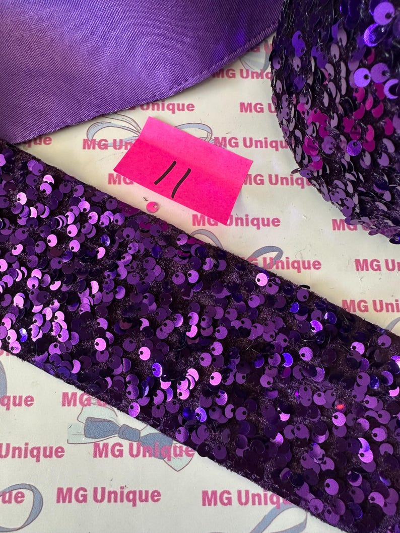 Op de afbeelding: Close-up van diverse paarse knutselbenodigdheden. Inclusief een breed paillettenlint, een satijnen lint en een bolletje paillettenmateriaal. Een roze prijskaartje met het nummer 11 is ook zichtbaar. De achtergrond heeft de tekst "MG Unique".