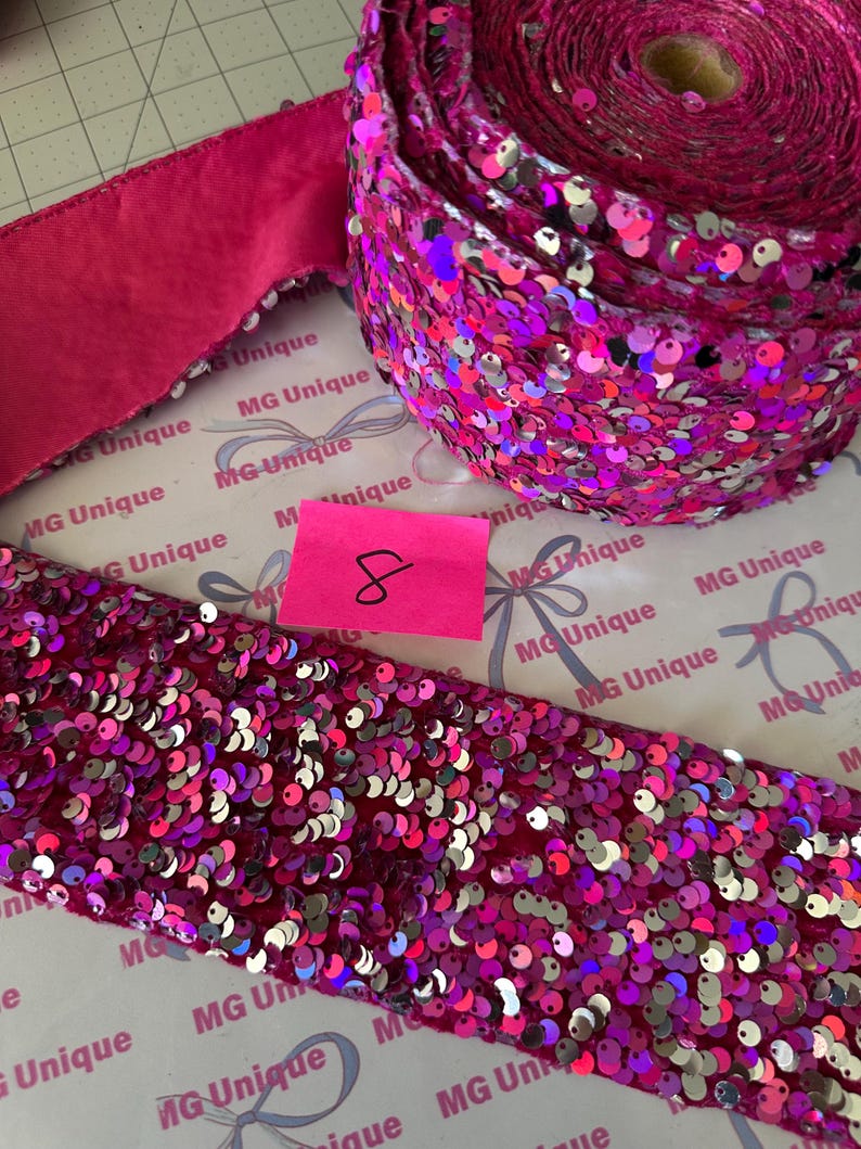 Op de afbeelding: Een rol levendig roze paillettenlint en een stuk paillettenlint worden getoond. Het lint is bedekt met glanzende, iriserende pailletten. Een kleiner stuk effen roze lint is ook zichtbaar. Een roze plakbriefje met het nummer 8 staat in de afbeelding.