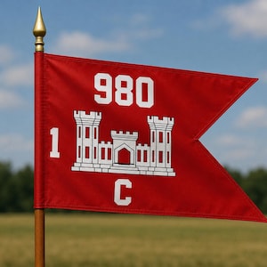 May include: A red swallowtail guidon flag featuring a white castle emblem, the number 980 at the top, the number 1 on the left, and the letter C at the bottom. The flag is attached to a wooden pole topped with a gold-colored metal spear finial.