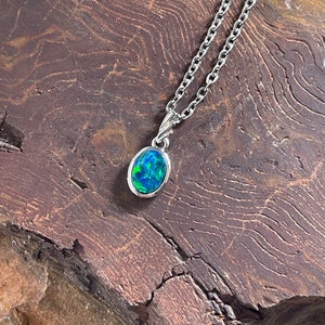 Puede incluir: Un collar de cadena de plata con un pequeño colgante ovalado con una ópalo verde y azul.