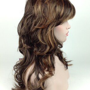 May include: A long, wavy brown wig with blonde highlights. The wig is styled with layers and a side parting.