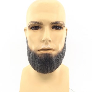 May include: A mannequin head with a bald, tan-colored scalp, brown eyebrows, and dark eyes. The mannequin has a full, gray beard. The background is plain white.
