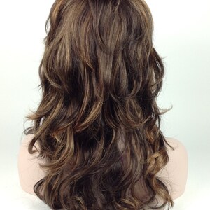 May include: A long, wavy brown wig with blonde highlights. The wig is styled in loose curls and falls to the shoulders.