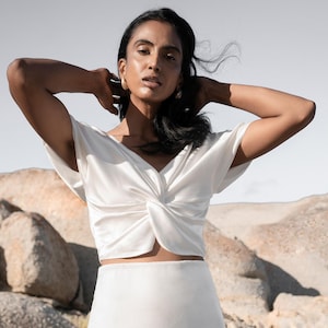 May include: A white crop top with a twist detail and a white maxi skirt.