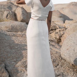 May include: A white satin top with a v-neck and short sleeves paired with a white satin maxi skirt.