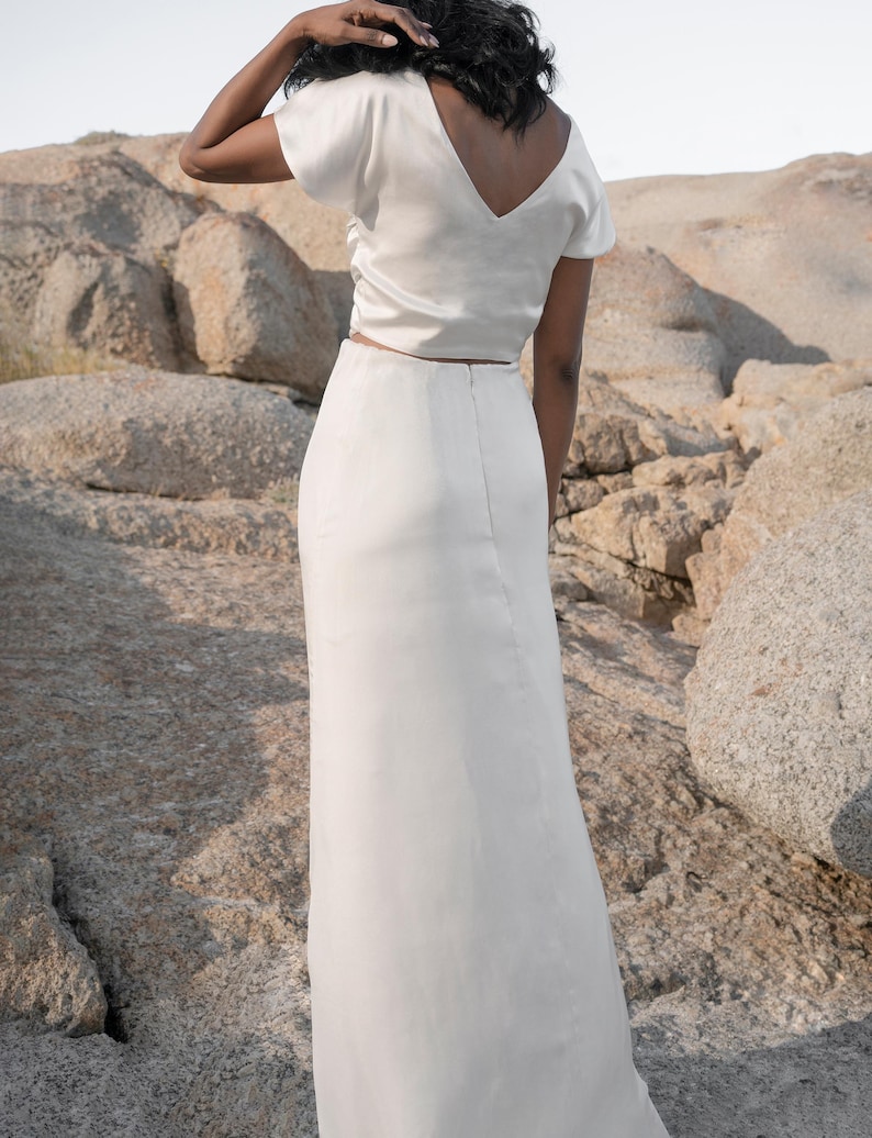 May include: A white satin top with a v-neck and short sleeves paired with a white satin maxi skirt.