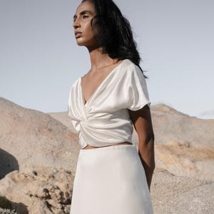 May include: A white satin top with a twist detail at the front and a matching white satin skirt.