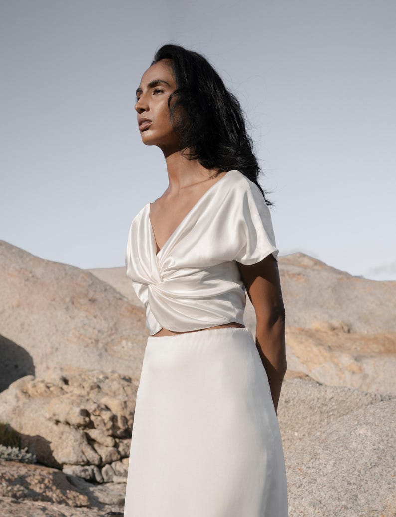 May include: A white satin top with a twist detail at the front and a matching white satin skirt.