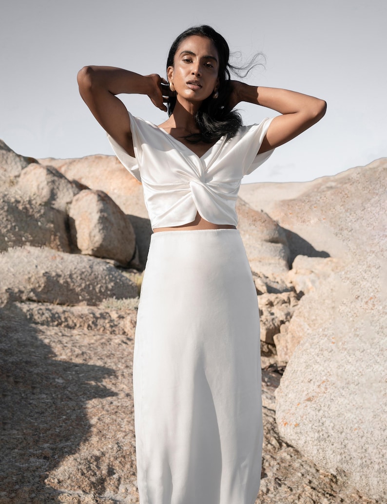 May include: A white crop top with a twist detail and a white maxi skirt.