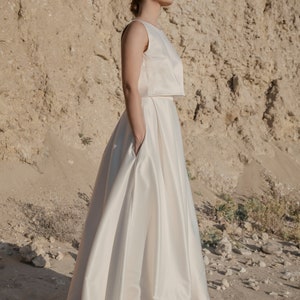 May include: A white sleeveless crop top and a white satin skirt. The skirt has a high waist and a flowing silhouette.
