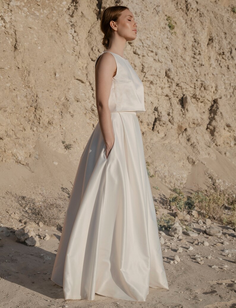 May include: A white sleeveless crop top and a white satin skirt. The skirt has a high waist and a flowing silhouette.