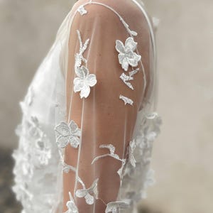 May include: White sheer lace overlay with floral embroidery. The lace has a delicate floral pattern with small white flowers.