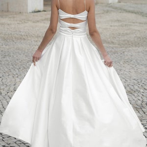 May include: A white satin wedding dress with a low back and a bow detail. The dress has a full skirt and a fitted bodice.