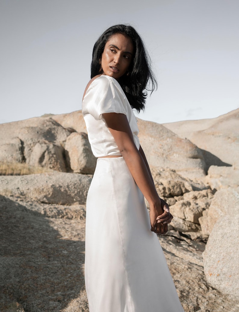 May include: A white satin top with short sleeves and a white satin skirt.