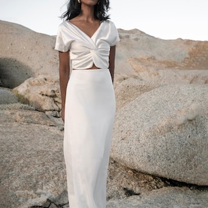 May include: A white satin top with a twist detail at the front and a matching white satin skirt. The skirt is a maxi length and has a simple design.