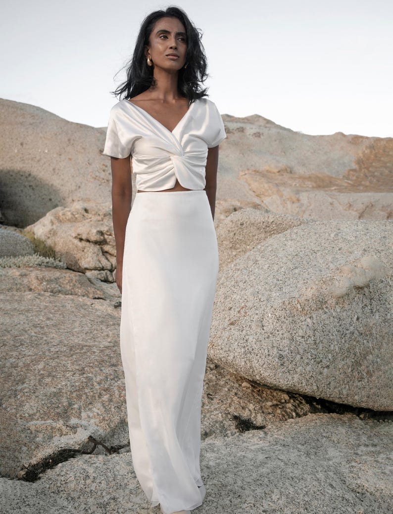 May include: A white satin top with a twist detail at the front and a matching white satin skirt. The skirt is a maxi length and has a simple design.