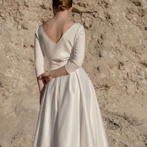 May include: A white satin wedding dress with a V-neckline and three-quarter sleeves. The dress has a fitted bodice and a flowing skirt.