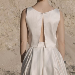 May include: A white satin dress with a low back and a fitted bodice. The skirt is full and flowing.