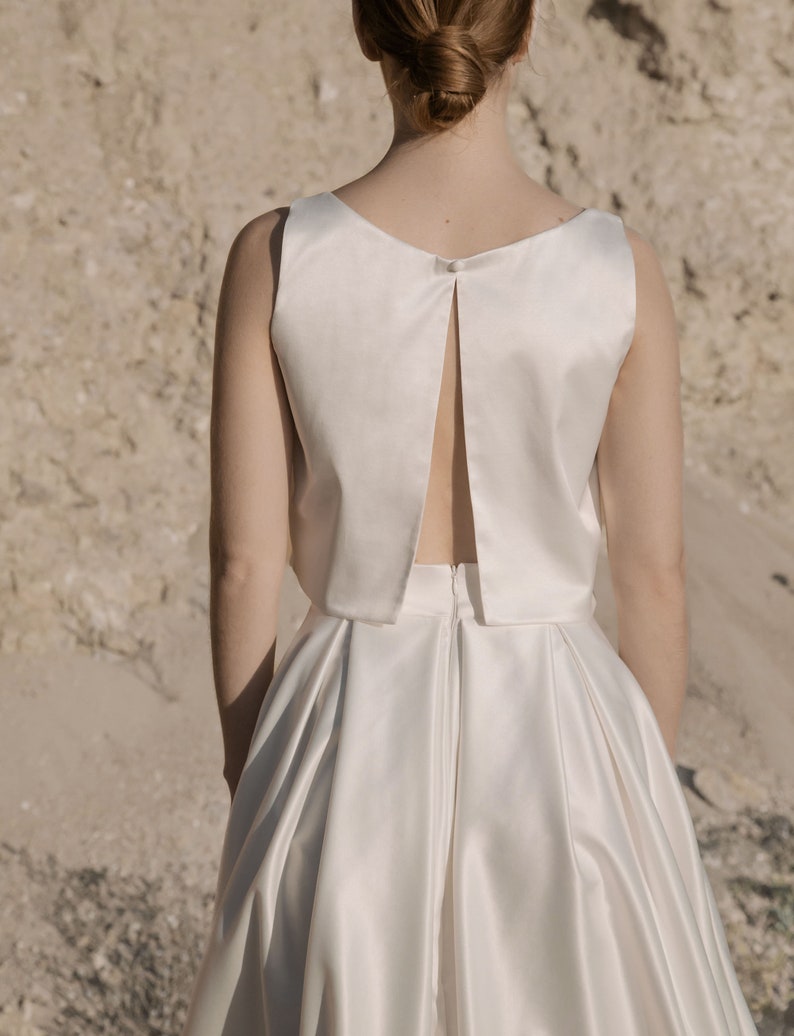 May include: A white satin dress with a low back and a fitted bodice. The skirt is full and flowing.