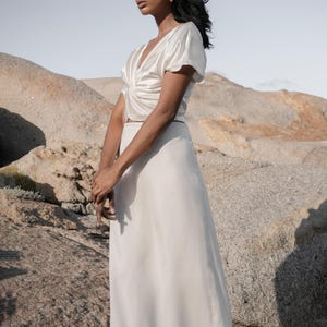 May include: A white satin top with a twist detail at the front and a white satin skirt.