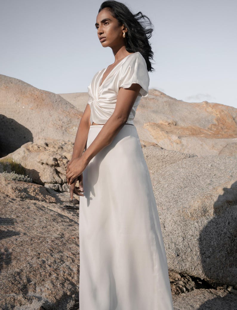 May include: A white satin top with a twist detail at the front and a white satin skirt.