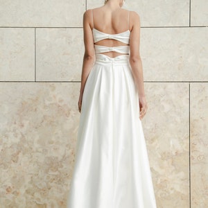 May include: A white satin dress with a low back and a bow detail. The dress has a fitted bodice and a flowing skirt.