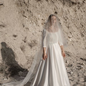 May include: A white wedding dress with a long veil. The dress has a fitted bodice and a flowing skirt. The veil is made of tulle and has a delicate lace trim.
