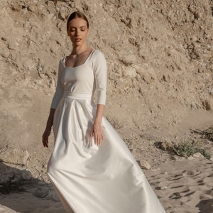 May include: A white satin wedding dress with a square neckline and three-quarter sleeves. The skirt is full and flowing.