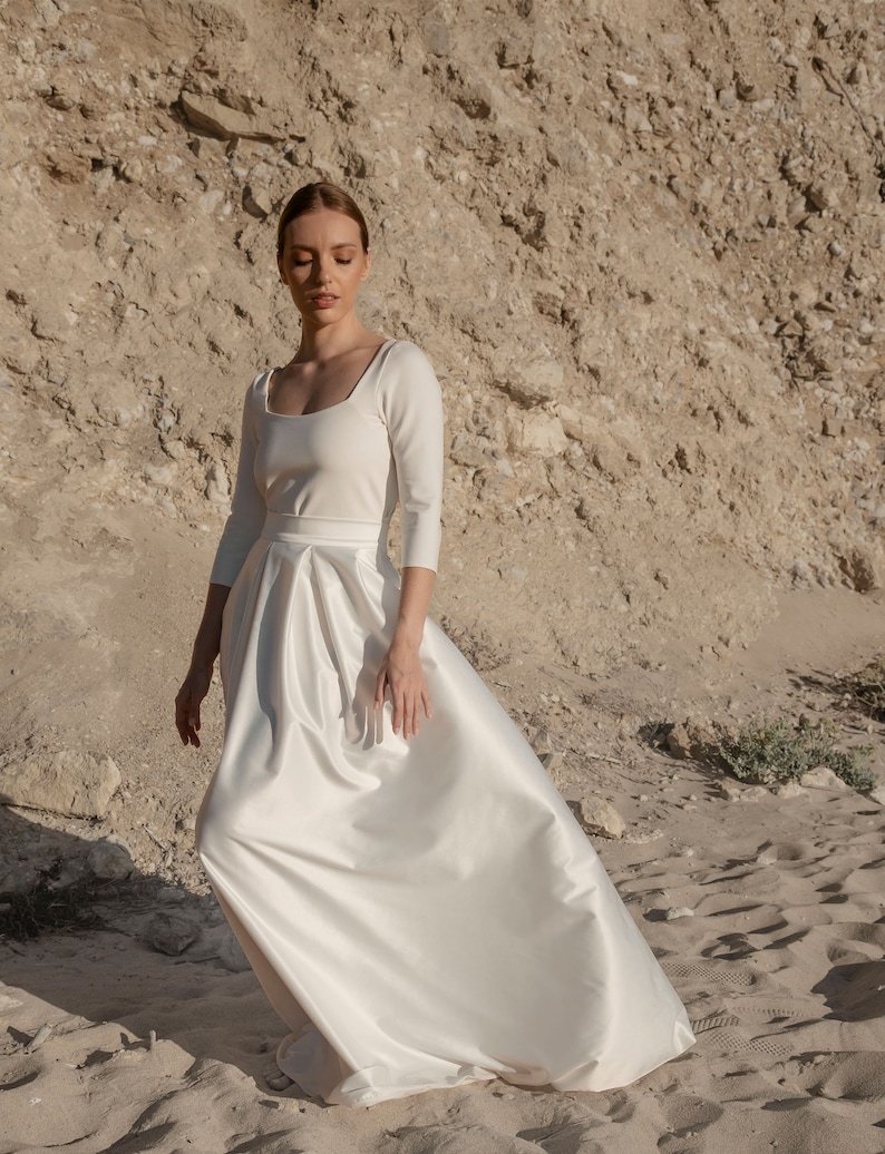 May include: A white satin wedding dress with a square neckline and three-quarter sleeves. The skirt is full and flowing.