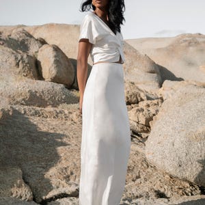 May include: A white satin top with a twist detail at the front and a matching white satin maxi skirt.