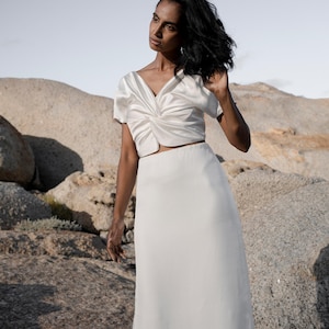 May include: A white crop top with a twist detail and a matching white maxi skirt.