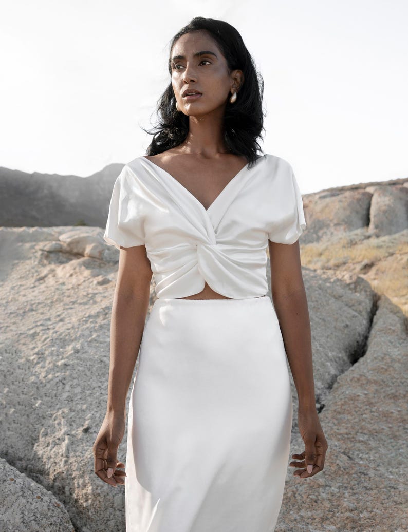 May include: A white satin top with a twist detail at the front and a matching white satin skirt.