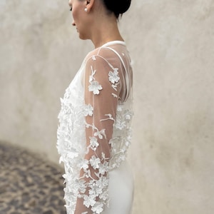 May include: A white sheer top with floral embroidery. The top has long sleeves and a fitted silhouette.