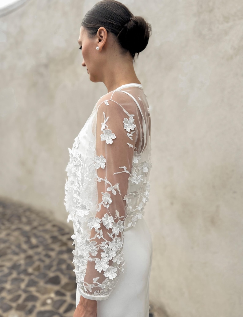 May include: A white sheer top with floral embroidery. The top has long sleeves and a fitted silhouette.