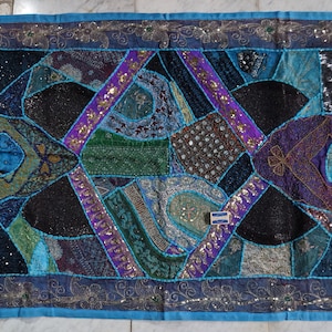 Puede incluir: Un tapiz de pared de patchwork colorido con un diseño geométrico. El tapiz está hecho de varias telas y está adornado con lentejuelas, cuentas y bordados. Presenta tonos de azul, morado, verde y negro.