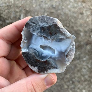 May include: A gray and white agate geode with a natural opening revealing a white and gray interior. The geode is smooth and has a rough exterior.