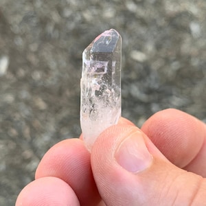 May include: A clear quartz crystal with a pink hue at the top. The crystal is pointed at the top and has a smooth, polished surface.