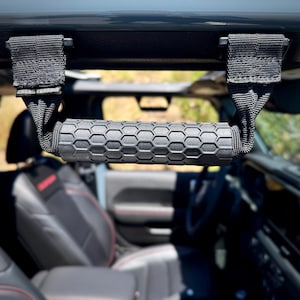 May include: Black grab handle with a textured, hexagonal pattern grip. The handle is attached to a black strap with the text "CROSS TERRAIN". The handle is mounted inside a vehicle.