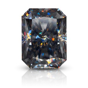 Puede incluir: Una piedra preciosa de corte radiante con un tono gris oscuro carbón. La piedra presenta una superficie compleja de múltiples facetas que refleja la luz, creando patrones geométricos nítidos y sutiles destellos prismáticos de color.