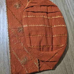 May include: A brown fabric hat with gold embroidery and a scalloped edge.