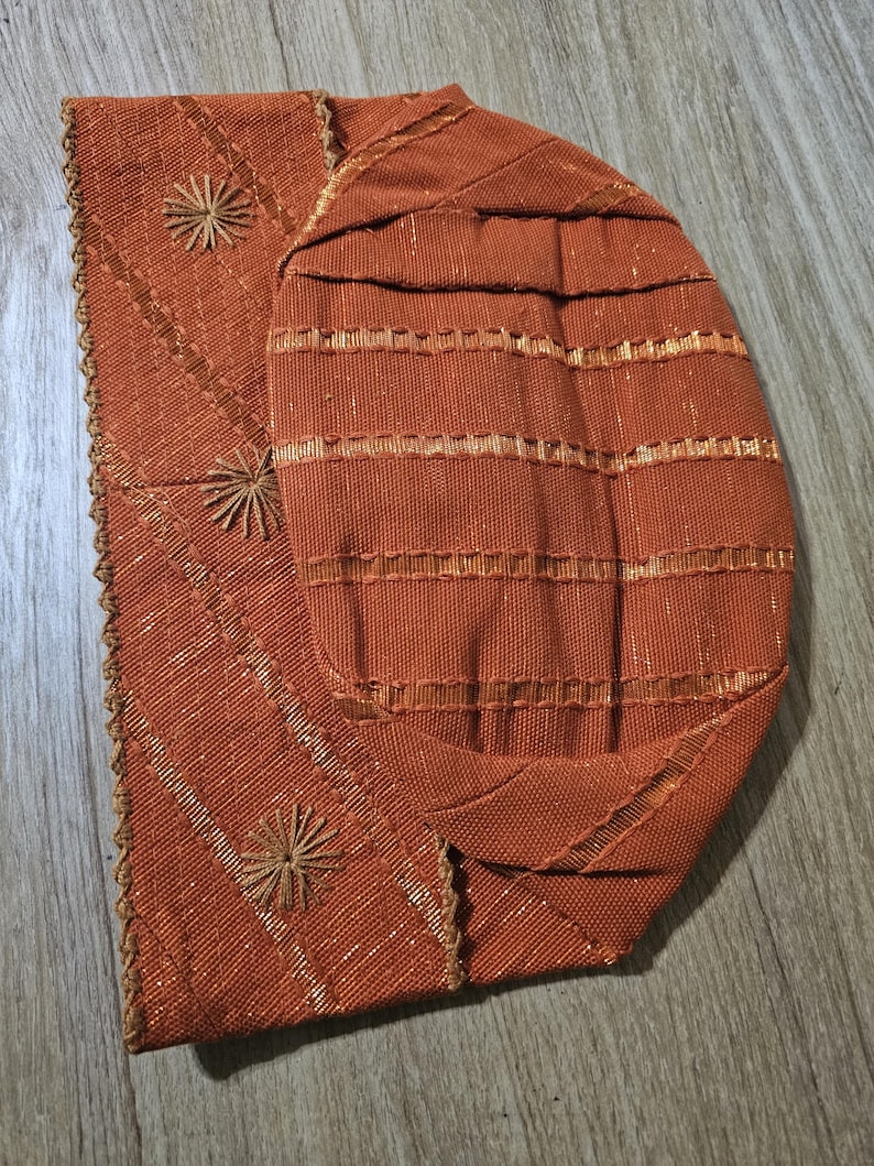 May include: A brown fabric hat with gold embroidery and a scalloped edge.