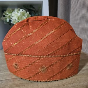 May include: A brown woven hat with gold accents and embroidered details. The hat has a rounded shape and a slightly pointed top.