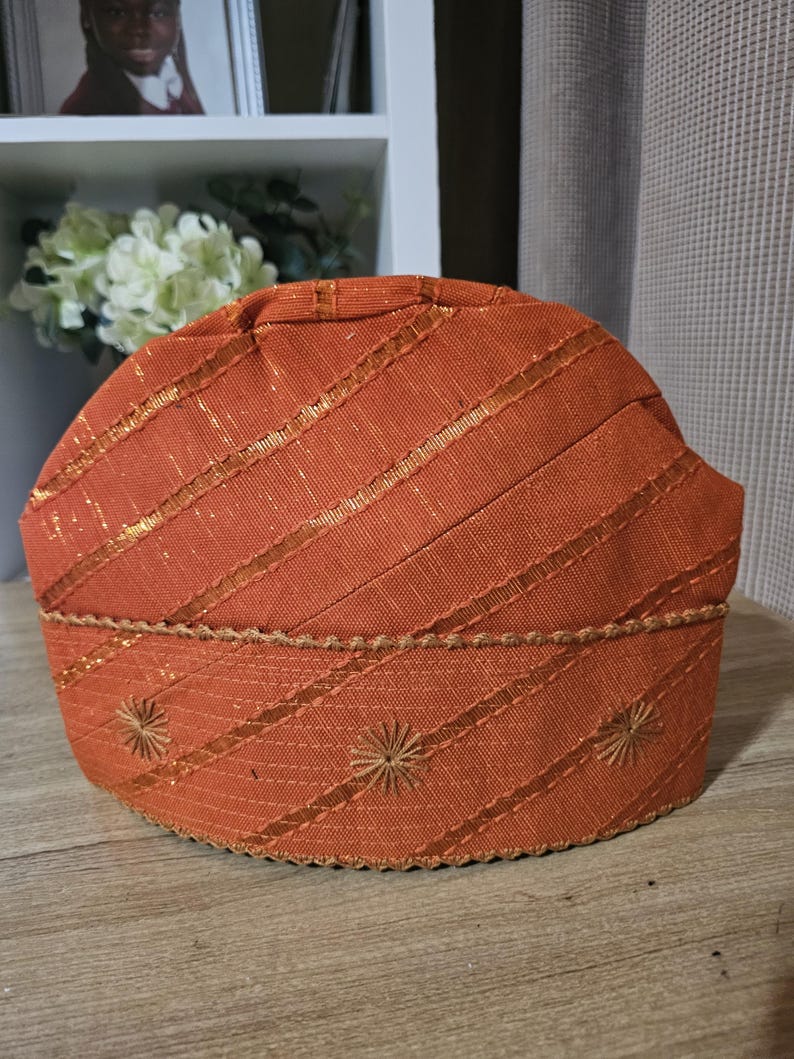 May include: A brown woven hat with gold accents and embroidered details. The hat has a rounded shape and a slightly pointed top.