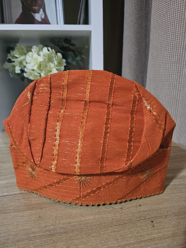 May include: A brown and gold striped fabric hat with a scalloped edge and embroidered stars.