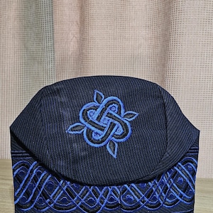 May include: A blue and black embroidered skullcap with a decorative design. The skullcap is made of a soft, textured fabric.