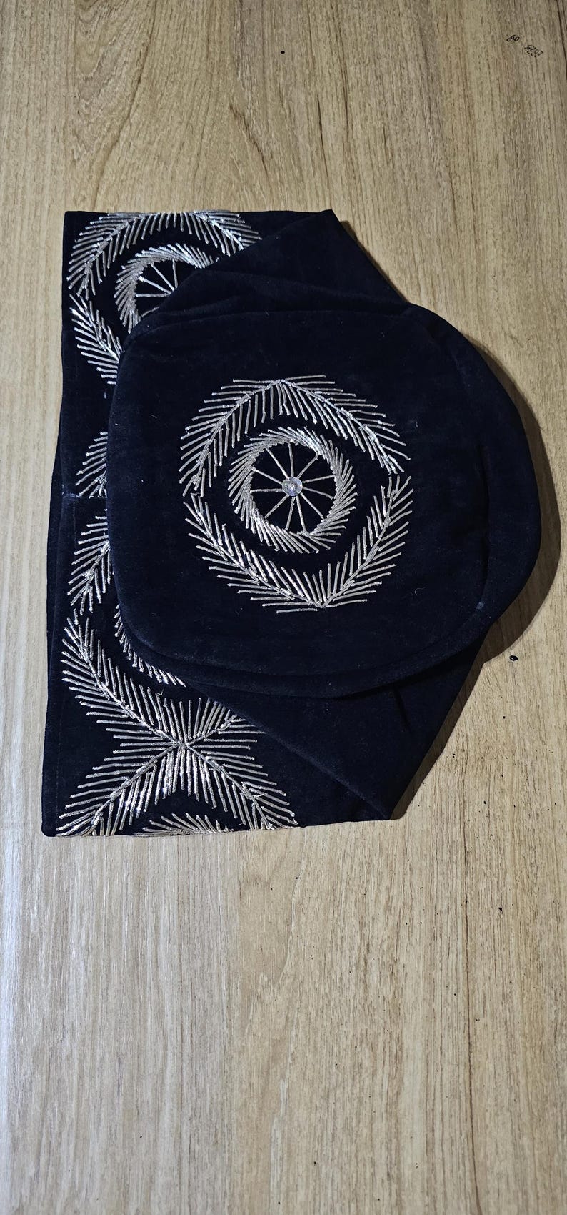 May include: Two black velvet fabric squares with silver embroidery. The embroidery is a circular design with a smaller circle in the center.