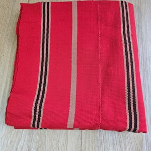 Può includere: Tessuto rosso con strisce nere e beige. Il tessuto è piegato a metà e si trova su una superficie di legno.